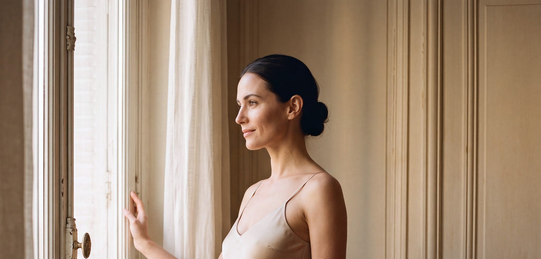 Une femme en robe de soie champagne regarde par la fenêtre d'un appartement parisien